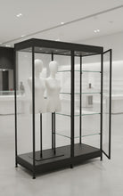 A Double mannequin with shelves to one side is displayed in a sleek black illuminated glass cabinet with an open door. Two headless white mannequins are inside, and the background is bright and spacious in a minimalist store.