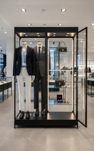 The Double mannequin with shelves to one side is displayed in an illuminated glass cabinet, showcasing two mannequins in formal business attire, with luxury accessories like handbags and watches arranged neatly on the nearby shelves.