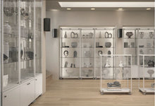 The Fusion Plus 5PLP Jewellery Glass Display Case features lockable doors and is ideal for displaying pottery, sculptures, or artifacts. With light wood floors, white walls, and overhead lighting, the room offers a clean, modern look.