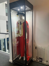 A Single Mannequin Showcase displays a ceremonial robe with a red cape, white fur trim, and black hat on a mannequin inside a lockable cabinet. A sign with text and photo is placed next to the case in the modern building.