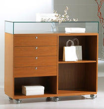 The Premier Lite 12.105B Double Wide Display Counter features lockable drawers, open shelves, a veneered wooden base, and wheels. Decorative branches, white boxes, and gift bags are displayed on and within the cabinet.
